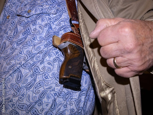 Obraz A man pulls his coat open to reveal a pistol concealed in a shoulder holster.