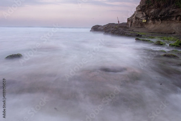 Fototapeta the beautiful view of a tropical beach in the morning, with white sand and coral rocks hit by ocean waves. Landscape images are taken with slow speed technique.