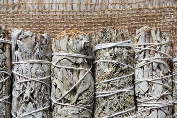 Fototapeta A top view image of several white sage smudge sticks lined up on a ripped burlap sack cloth.