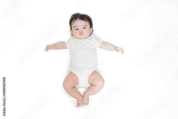 Obraz 白いロンパースを着て仰向けに寝るカメラ目線の赤ちゃんを俯瞰撮影