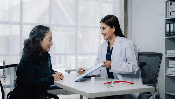 Fototapeta Doctor and Patient Consultation: A friendly and professional female doctor discusses medical records with a senior patient, creating a sense of trust and care in a modern office setting.  