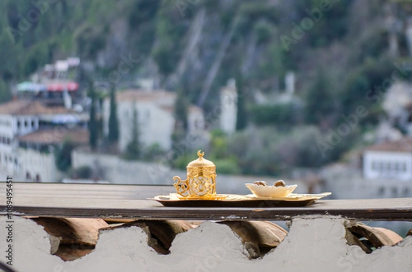 Fototapeta A traditional Turkish coffee set, made of gold and porcelain, rests on a wooden tray. The background is slightly blurred, creating a sens