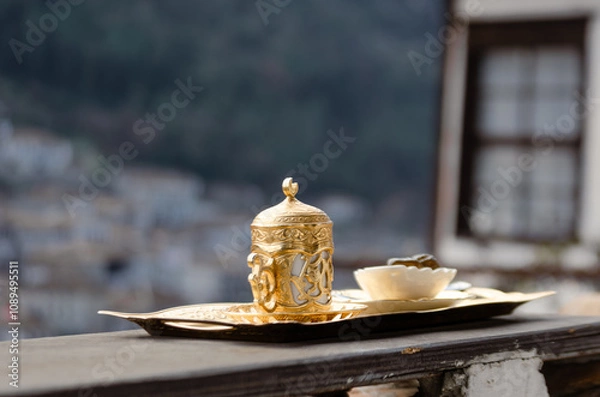 Fototapeta A traditional Turkish coffee set, made of gold and porcelain, rests on a wooden tray. The set is placed on a balcony overlooking the picturesque town of Berat in Albania