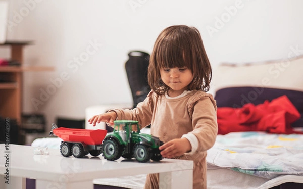 Obraz A little girl is playing with a tractor toy
