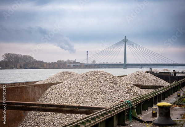 Obraz Industrial Landscape with Barge, Bridge, and Smoke Stack - River, Waterway, Cargo, Transportation, Logistics, Industry, Factory, Pollution, Environment, Climate Change, Urban, Cityscape, Bridge, Const