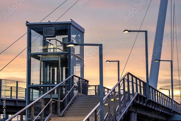 Obraz Modern Pedestrian Bridge at Twilight - Urban Metro Station Infrastructure, Architecture, Cityscape, Transportation, Pathway, Stairs, Elevator, Light, Dark, Contrast, Sky, Sunset, Twilight, Evening