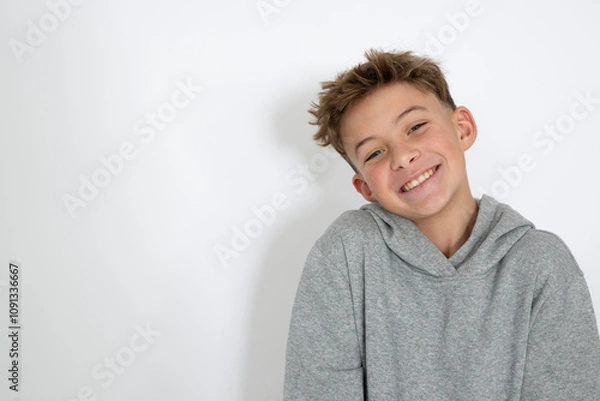 Fototapeta cool young 12 year old boy with grey hoody sweater posing in front of white background, having fun