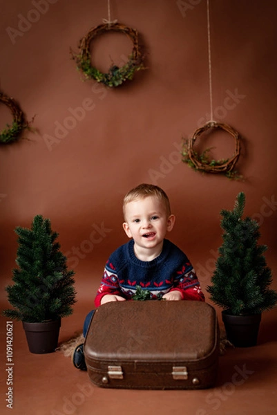 Fototapeta beautiful boy child 3 years old on brown background with christmas tree and an old suitcase