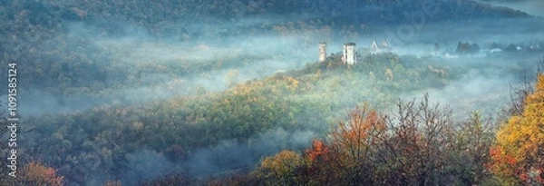 Obraz wide-angle panorama landscape with tales of morning fog between forests hills and ruins of medieval castle in autumn morning