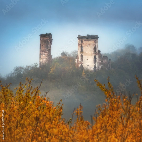 Obraz view to ruins of two towers of medieval castle in fog and golden autumn leaves on foreground