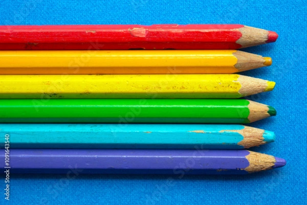Fototapeta close up of colored wooden pencils in a row, on blue background. top view