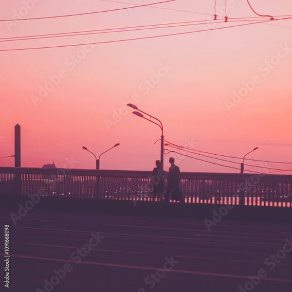 Fototapeta A young couple in love walks across a bridge, with lanterns and wires in the background. The sky is a soft pink, creating a romantic atmosphere.