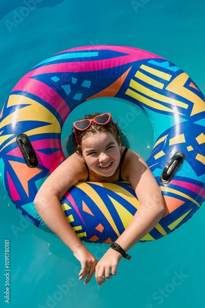 Fototapeta cute happy girl 12 years old swims in a pool with blue water in a bright circle. High quality photo