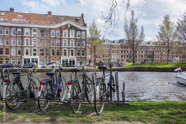 Fototapeta Several bikes on the parking near the grand canal in Amsterdam with several brown buildings as background