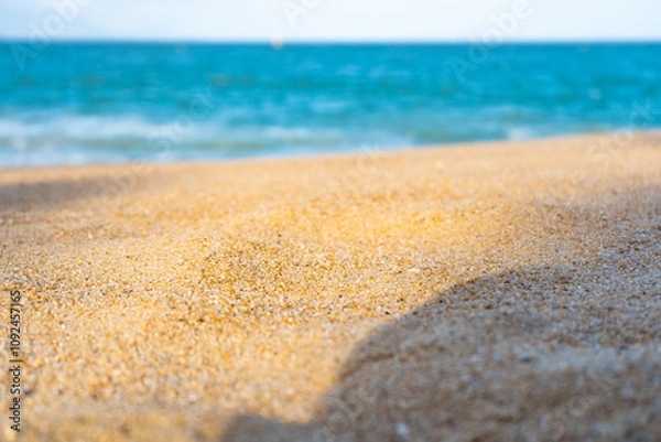 Fototapeta Close-up view of a sandy beach with a blurred turquoise sea in the background. The central part of the image is perfect for placing objects or text. A great choice product showcase