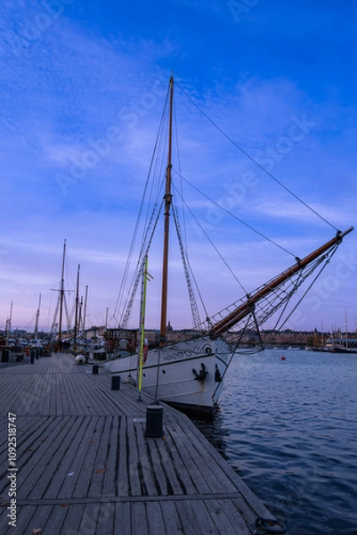 Fototapeta A serene sailboat anchored in the tranquil waters of Stockholm's harbor at sunset