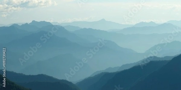 Fototapeta Elegant mountain range with soft blur on distant peaks and valleys gentle blue hue blending into green tones subtle cloud formations, scenic views, atmospheric perspective