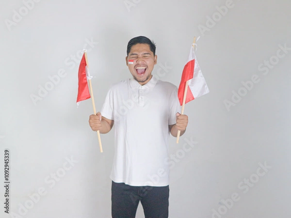 Obraz Excited young Asian man celebrate Indonesian independence day on 17 August by holding the Indonesian flag isolated over white background