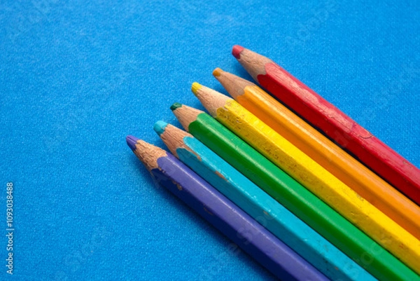Fototapeta close up of colored wooden pencils in a row, on blue background. top view