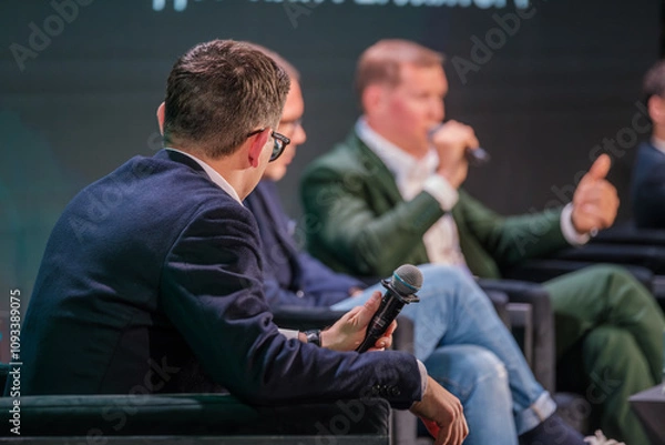 Obraz Corporate leaders engaging in discussion on stage with microphones and audience. Professional conversation during formal event.