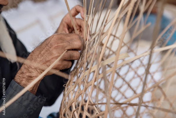 Obraz Old man is knitting weaving traditional basket from palm leaves, hands in frame