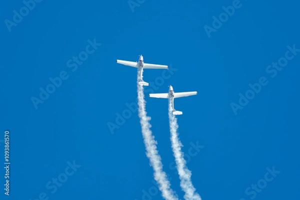 Fototapeta Stunt aerobatic plane performing stunts in blue sky with smoke trail. Concept of teamwork, collaboration, coordination, trust, precision, difficulty, challenge, speed, synergy