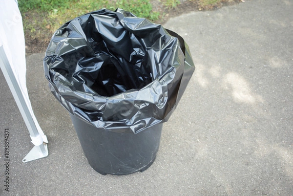 Obraz Garbage bucket. Black bag in the bucket. A trash can on the street.