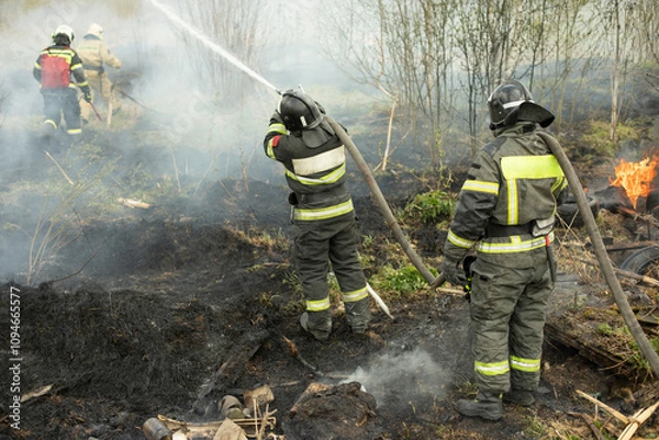 Obraz Two rescuers extinguish flames. Firefighters are fighting fire. Large hose with water pressure.