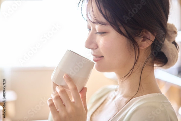 Fototapeta カップを手に持ち飲み物を飲む若い女性。