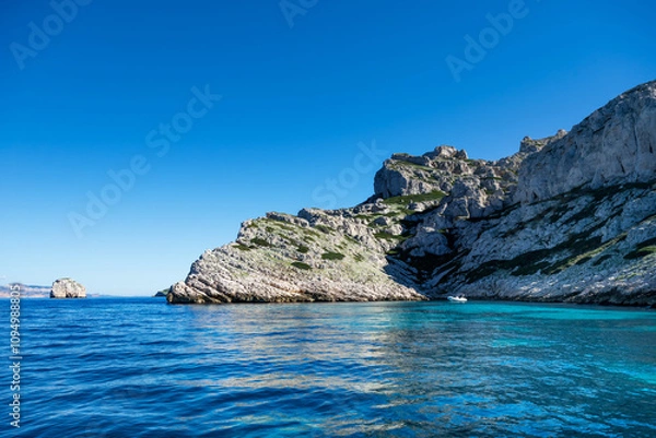 Fototapeta A bay of a rocky island in the Mediterranean with a pleasure motorboat in turquoise water on a sunny day.