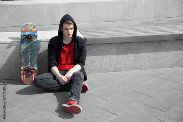 Obraz young skater resting on ground, skate board stands near