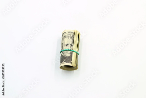 Fototapeta A bundle of American dollar bills surrounded by a green rubber band on a white background.