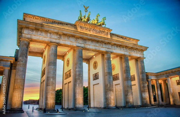 Fototapeta Built in 1873, the sandstone Brandenburg Gate, the symbol of German unity, has its fluted, Doric columns, lighted for the upcoming evening at blue hour in Berlin, Germany on a summer evening.
