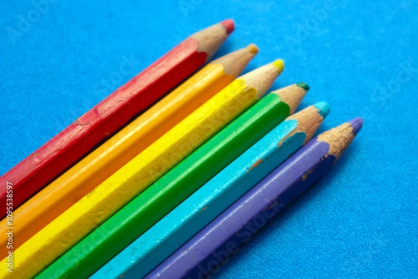Fototapeta close up of colored wooden pencils in a row, on blue background. top view