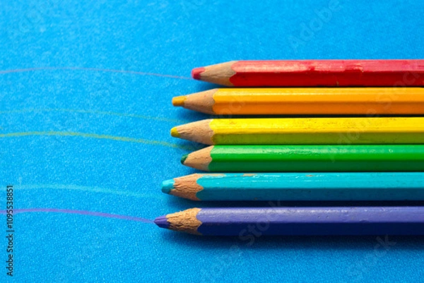 Fototapeta close up of colored wooden pencils in a row, on blue background. top view