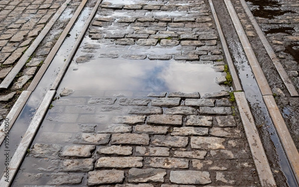 Obraz iron train track in perspective on stone cobblestone terrain with sky reflected in rainwater puddle