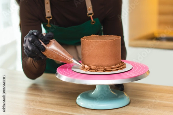 Fototapeta The process of a confectioner applying chocolate cream from a pastry bag onto a cake.
