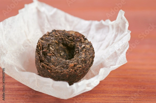 Obraz Unpacked dry pressed pu erh tea leaves briquette closeup on red wooden table