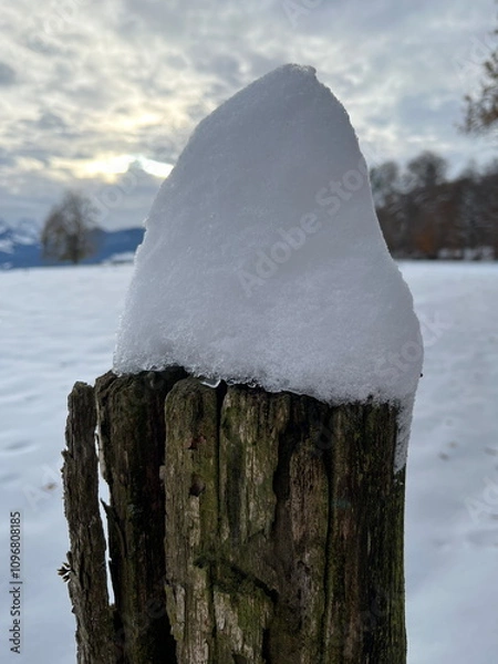 Obraz Closeup of fence post with snow on top, trees and sky in the background