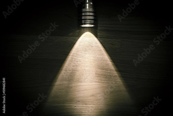 Obraz Flashlight and a beam of light in darkness. A modern led light with bright projection on dark wood table. Surface with copy space.