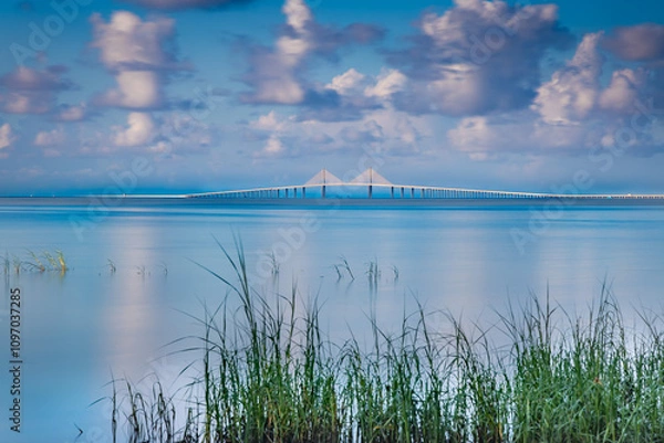 Fototapeta A serene waterscape features the long Sunshine Skyway bridge from Pinellas Point Park St Petersburg Florida The bridge stretching across a calm blue expanse, with wispy clouds scattered across the sky