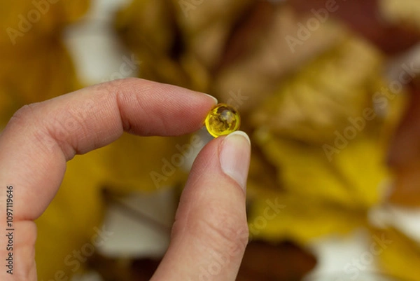 Fototapeta Concept of autumn supplementation. Closeup of a vitamin D capsule and yellow leaves.