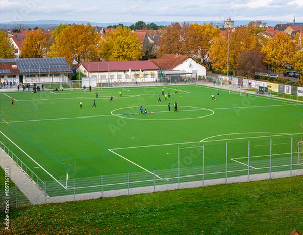 Obraz Soccer players practice on a vibrant field surrounded by autumn foliage in a small town