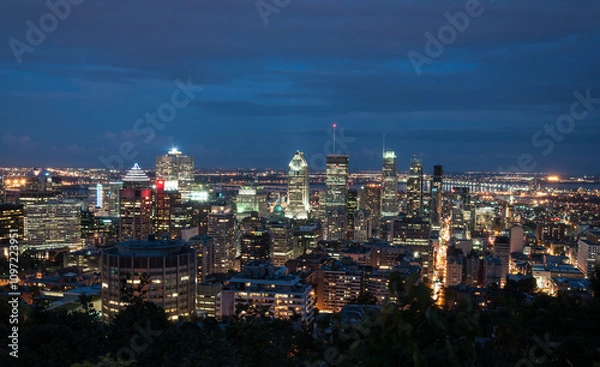 Obraz Stunning nighttime view of downtown Montreal, Canada, with illuminated skyscrapers and vibrant city lights under a deep blue sky. Perfect for urban and travel themes.