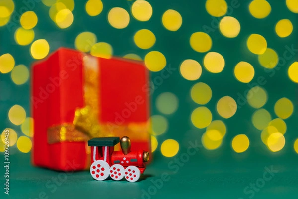 Fototapeta Photo of Christmas trains with a selective focus. Christmas decorations. Christmas background. Bright bokeh. Green background. One wooden locomotive on a green background. Red gift box on background.