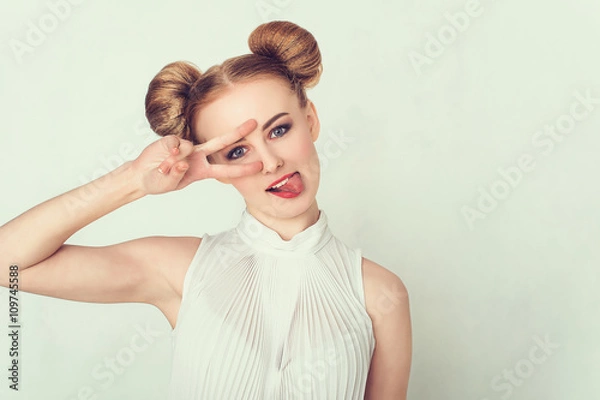 Fototapeta Beautiful girl with funny hairstyle makes peace sign hands, smiling and showing tongue.