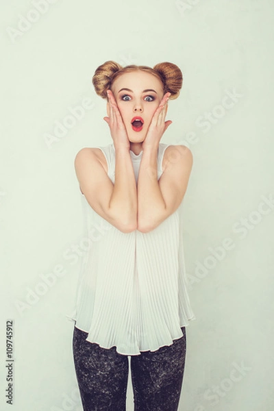 Fototapeta Portrait of surprised beautiful girl with funny hairstyle holding her head in amazement and open-mouthed. 