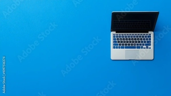 Fototapeta Laptop on Blue: A sleek silver laptop with a black screen rests on a vibrant blue background, creating a clean and modern visual. The image is perfect for showcasing technology, productivity.