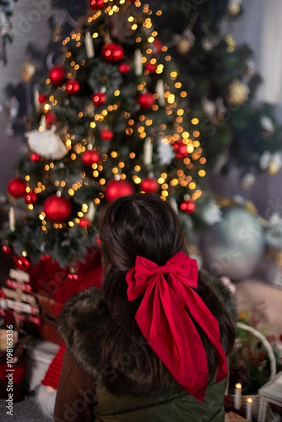 Fototapeta Dark-haired girl with red ribbon in front of a Christmas tree with light