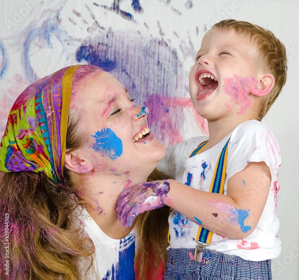 Fototapeta Mother and son paint the walls. Child himself dirty in the paint and looks into the camera. Child has fun and stain the wall. Children's creativity. Art for baby.